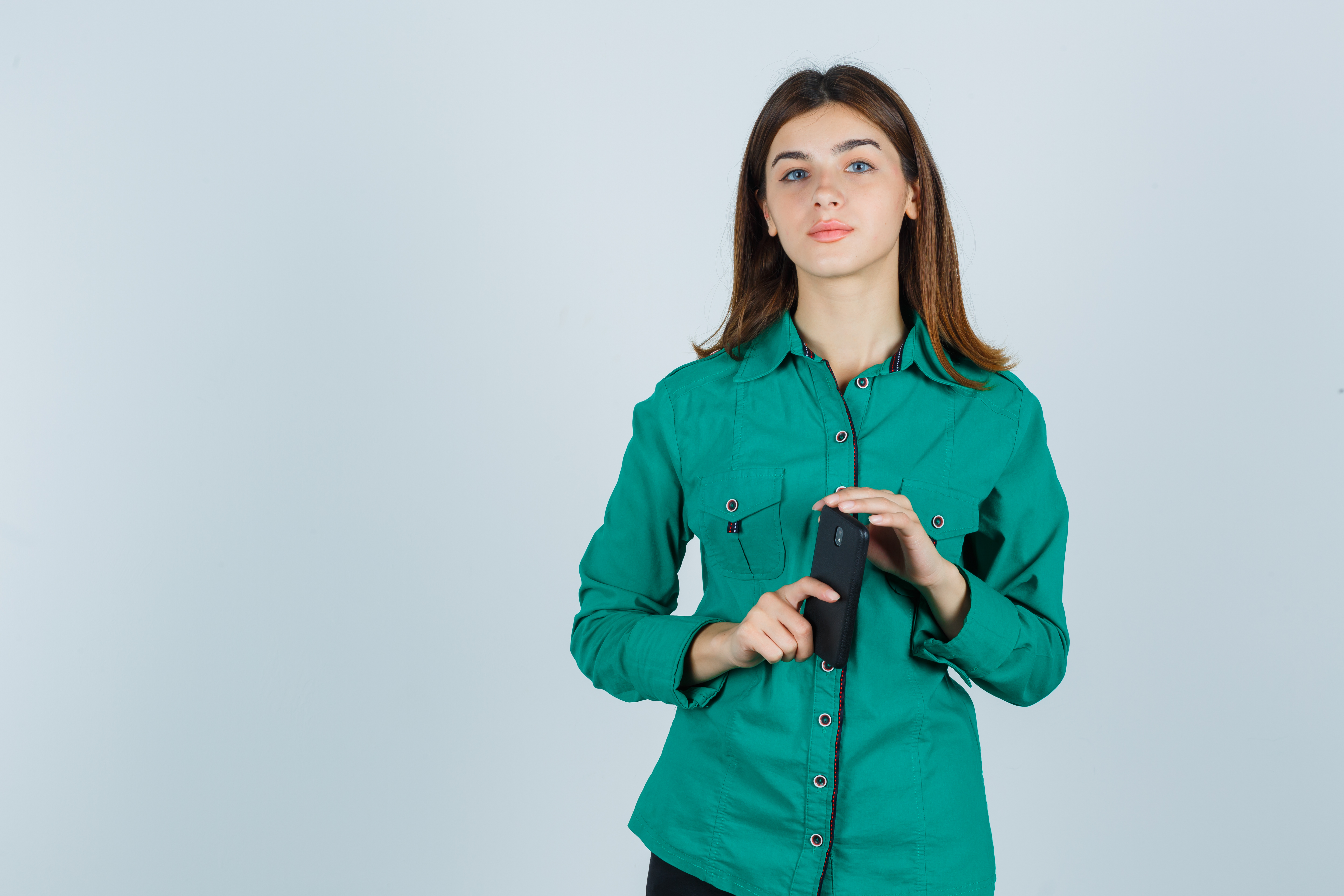 young lady holding mobile phone in green shirt and looking sensible. front view.